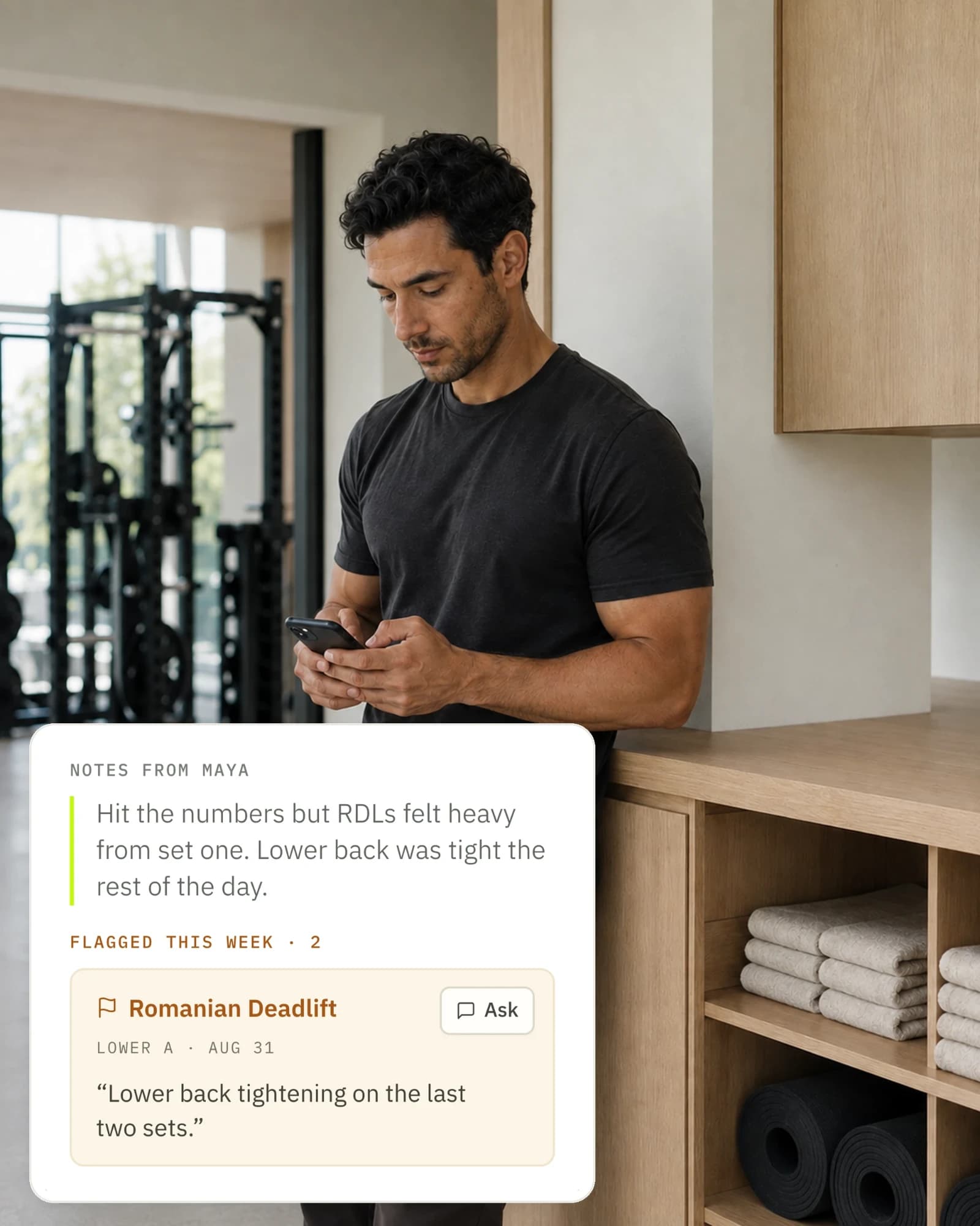 A coach in a gym reading a client's check-in on his phone: her notes about heavy Romanian deadlifts and a tight lower back, with the exercise she flagged that week beside them